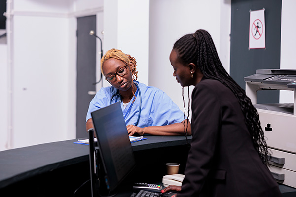 A woman in scrubs looking over paperwork with another woman in a medical setting