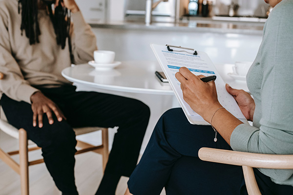 Cropped faceless image of a man talking around a table with and a woman who is looking at a clipboard